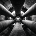 Black and white photo of a circular concrete structure with pipes converging towards the center.